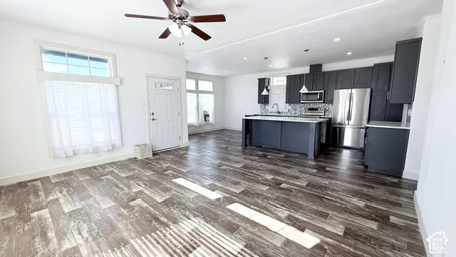 Open-concept living space featuring wood-finish flooring, a contemporary kitchen with dark cabinetry, stainless steel appliances, and an island with pendant lighting