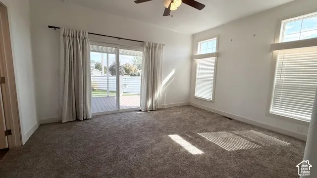 Carpeted room with a ceiling fan, sliding glass door, and multiple windows