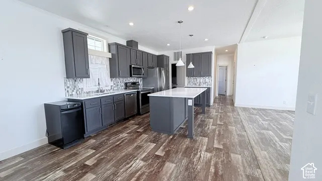 Kitchen featuring dark gray cabinetry, stainless steel appliances, a center island with pendant lighting, a tile backsplash, and wood-finish flooring