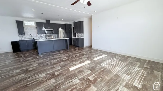 Kitchen featuring dark cabinetry, stainless steel appliances, a center island, and wood-finish flooring