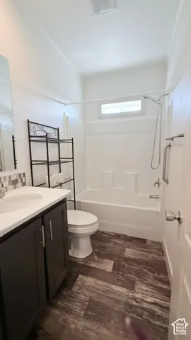 White bathtub and shower combination with a small transom window, dark wood-finish flooring, and a single vanity with a white countertop and dark cabinetry