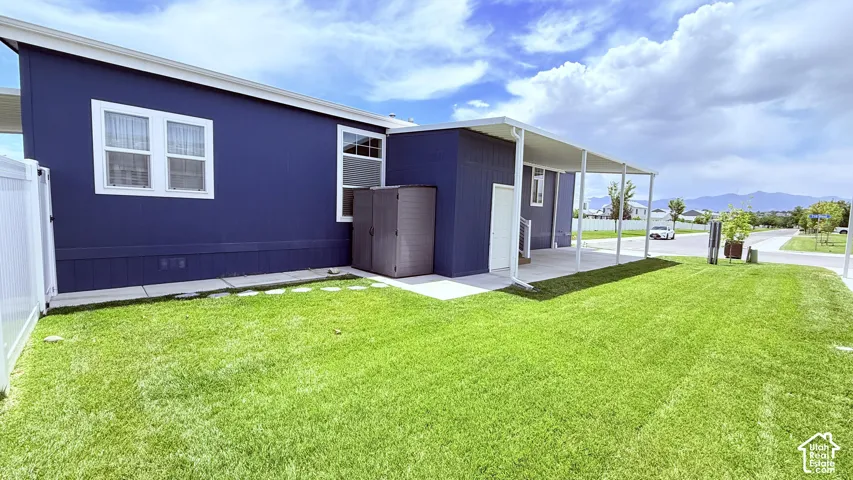 Included shed, expansive green lawn bordering the property, featuring a white fence and concrete patio with an extended white awning