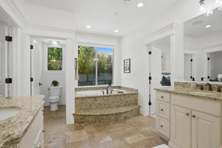 Spacious bathroom featuring a built-in soaking tub with stone surround, dual vanities with stone countertops, recessed lighting, and tile flooring