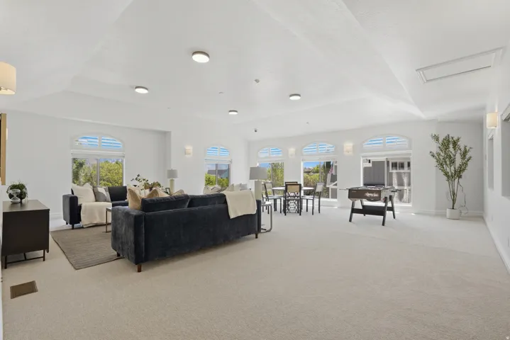 Spacious room featuring vaulted ceilings, recessed lighting, arched windows with plantation shutters, light-toned carpeting, and white wall finishes