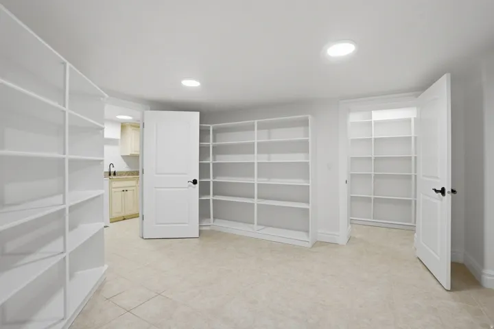 Spacious room featuring extensive built-in white shelving, light tile flooring, and recessed ceiling lighting