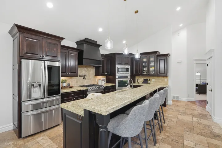 Spacious kitchen featuring dark wood cabinetry, stainless steel appliances, a large island with stone countertop, tile flooring, and vaulted ceilings