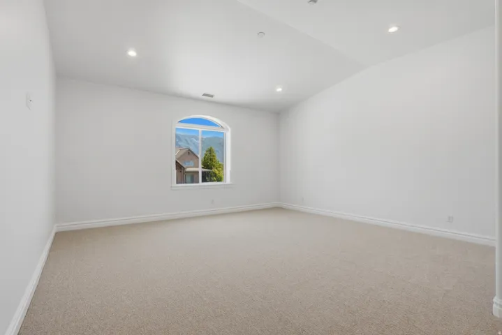 Spacious room featuring neutral carpet flooring, bright white walls, recessed ceiling lighting, and a large arched window framing mountain scenery