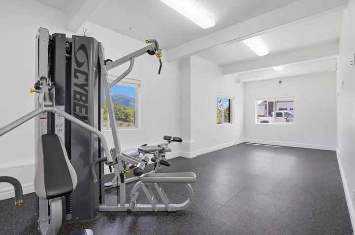 Dedicated fitness room with rubberized flooring, white walls, and exposed ceiling beams