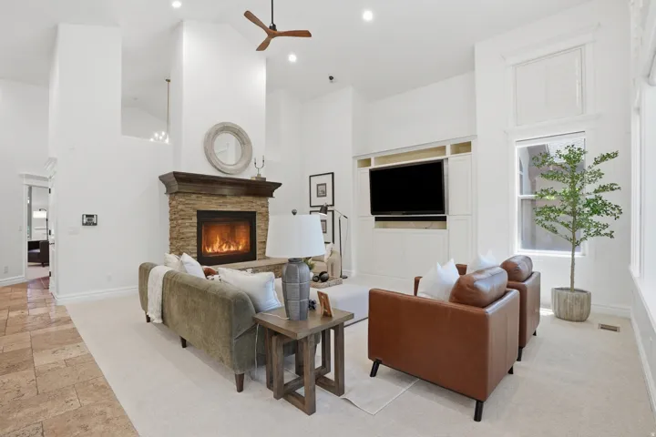 Spacious living area featuring vaulted ceilings, a stone-faced fireplace with a substantial wood mantel, recessed lighting, and a ceiling fan