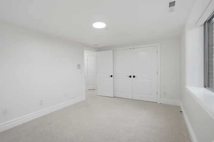 Carpeted interior space featuring a recessed ceiling light, white baseboards, and white double doors with matte black hardware