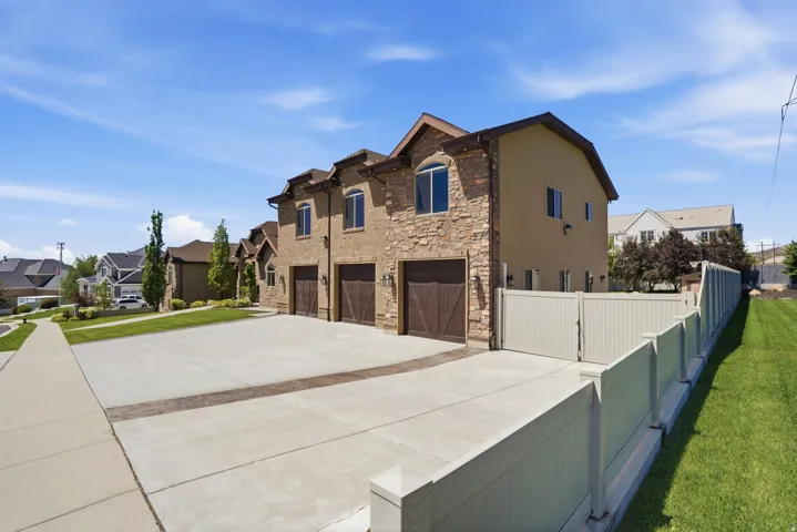 Stone and stucco exterior with three wood-finish garage doors, featuring an expansive concrete driveway and a full privacy fence