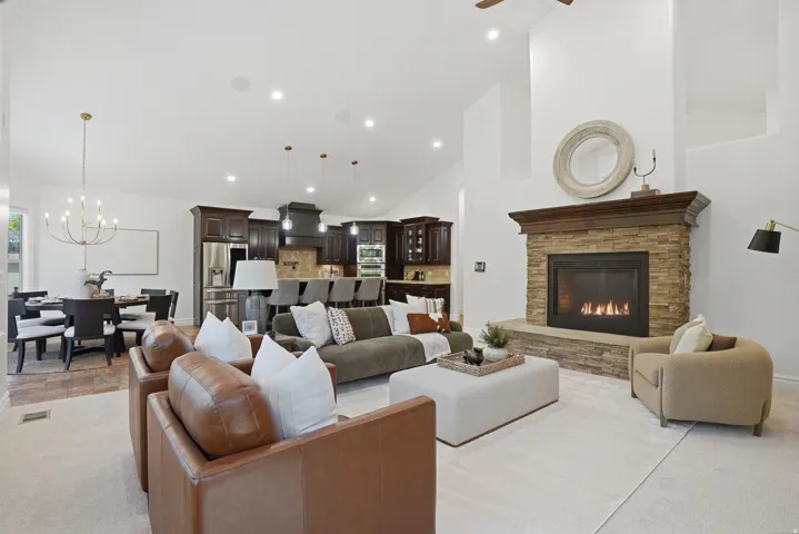 Spacious living area featuring a stone-clad fireplace with a wood mantel, high vaulted ceilings, and recessed lighting