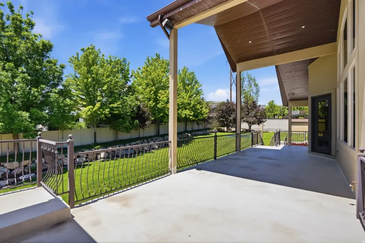 Expansive covered patio with concrete flooring, supported by a substantial pillar, and featuring a decorative metal railing