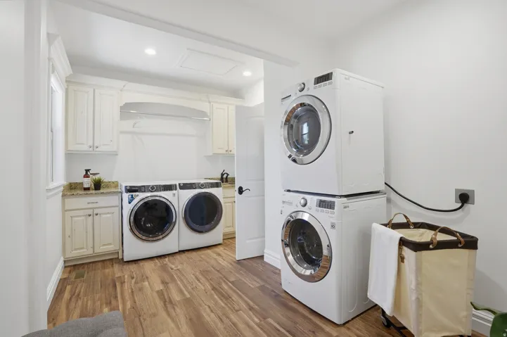 Laundry area featuring wood-finish flooring, white cabinetry, granite-finish countertops, and a white sink with a dark faucet