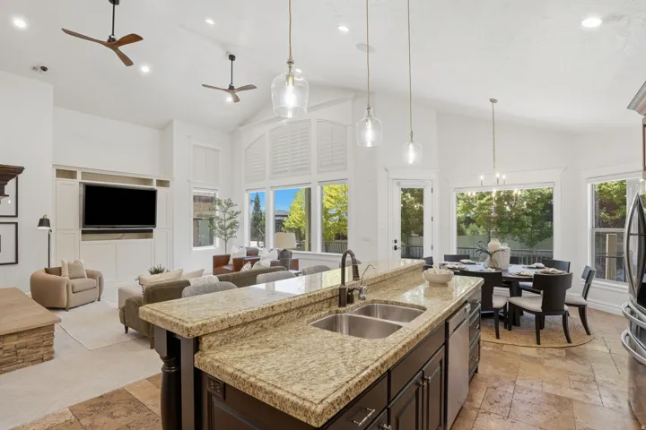 Open-concept living space featuring a kitchen island with dual sinks, granite countertops, and dark wood cabinetry