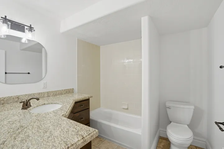 Bathroom featuring a wood-finish vanity with a granite-style countertop, undermount sink, and bronze-finish faucet