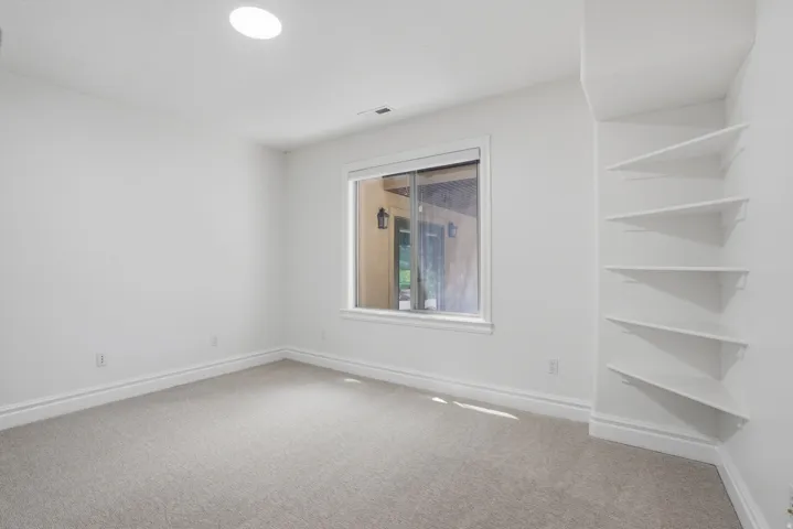 Carpeted room featuring a single window with white trim, built-in corner shelving, white baseboards, and a recessed ceiling light