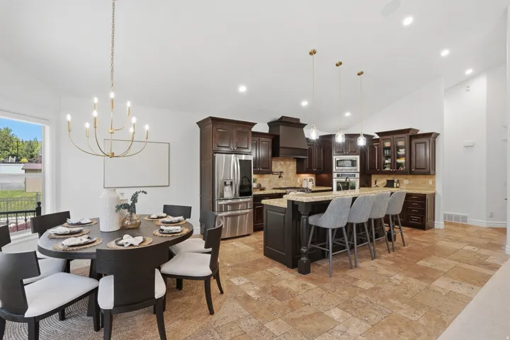 Open-concept kitchen and dining area featuring rich wood cabinetry, stainless steel appliances, a center island with bar seating, and natural stone tile flooring throughout
