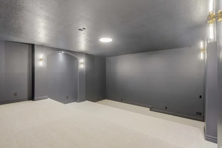 Spacious room featuring light-colored carpeting, dark gray walls, and a recessed archway with sconce lighting