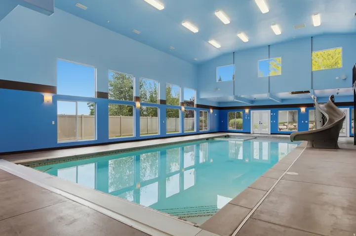 Indoor swimming pool featuring a built-in spa, dark gray waterslide, multiple large windows, and transom windows