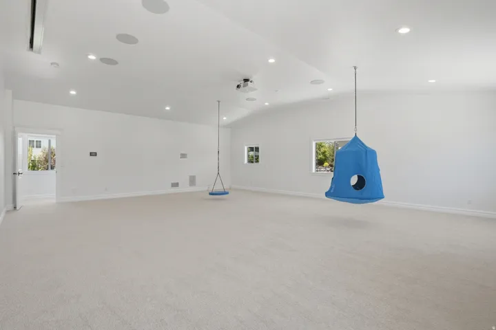 Spacious room featuring vaulted ceilings, recessed lighting, neutral carpeting, and multiple windows