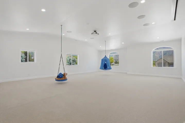 Expansive carpeted room featuring a vaulted ceiling with recessed lighting and integrated ceiling speakers