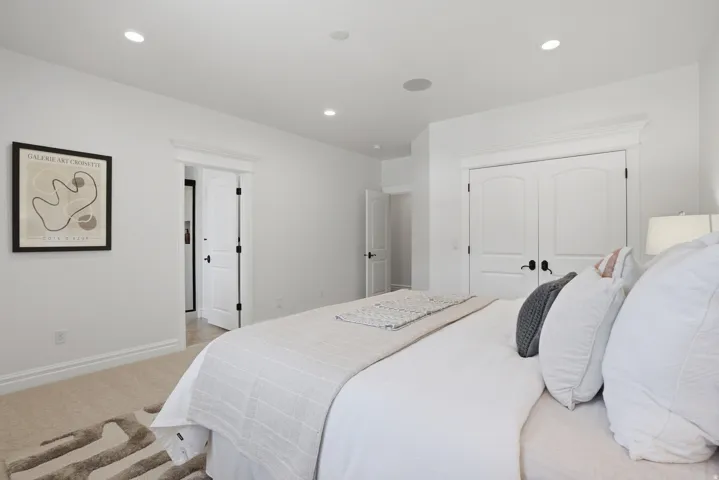 Bedroom featuring recessed lighting, light-colored carpet, white walls, and a pair of white arched panel doors with matte black hardware