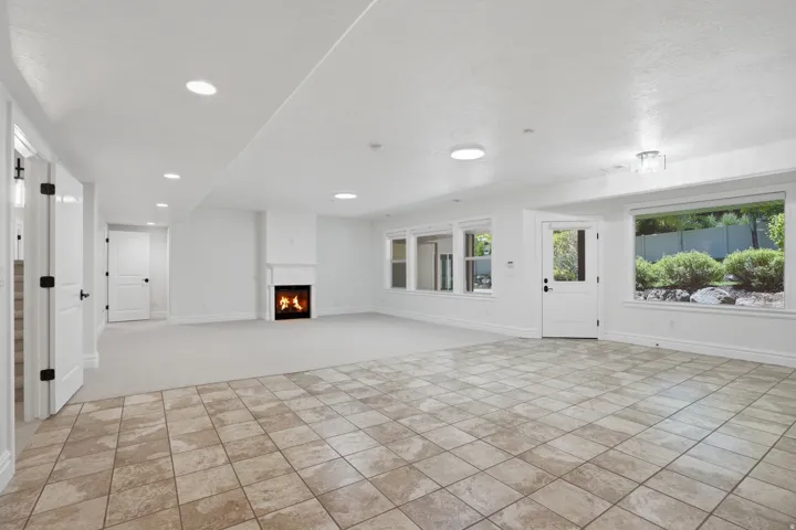 Spacious living area featuring multi-toned square tile flooring, neutral carpeting, a white mantel fireplace, multiple windows with white trim, and recessed lighting