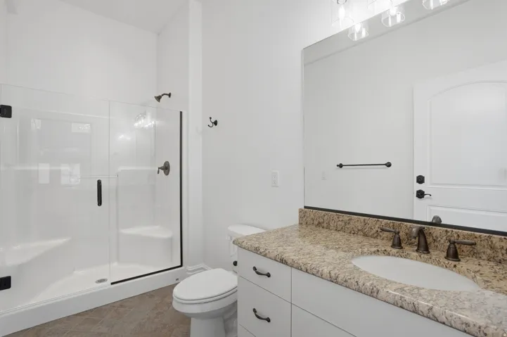 Spacious bathroom featuring a glass-enclosed shower, a vanity with a granite countertop, and a large wall-mounted mirror