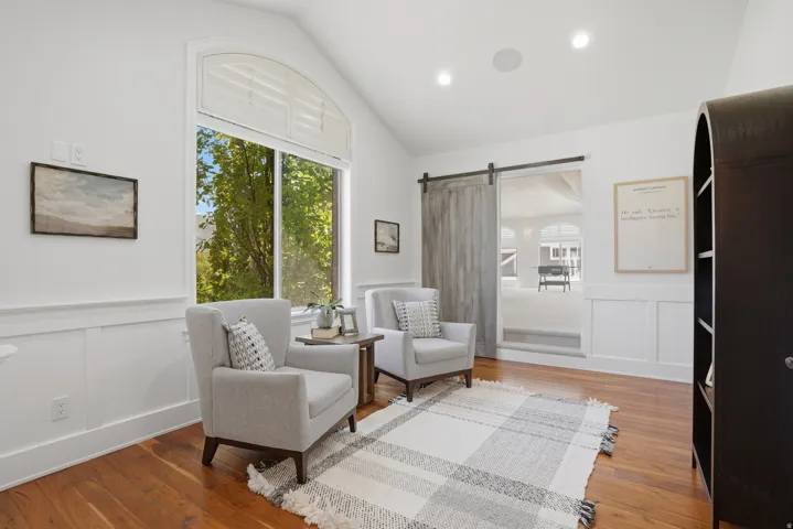 Vaulted ceiling room featuring rich wood-finish flooring and white wainscoting