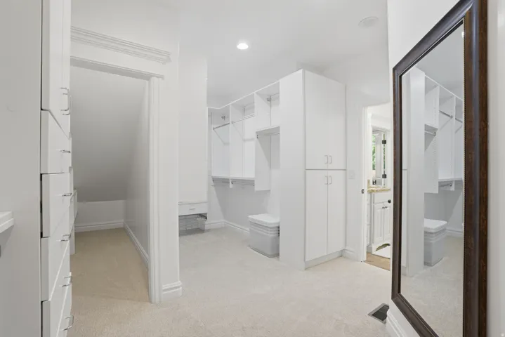 Spacious walk-in closet featuring built-in white cabinetry, integrated shelving, and soft carpeting