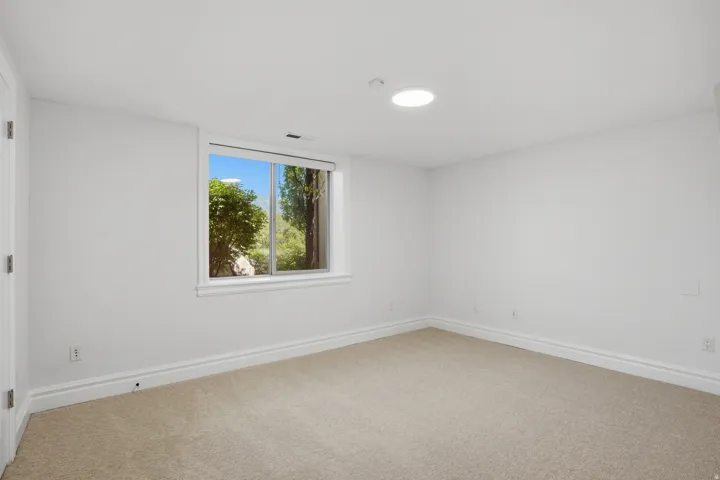 Bright room with neutral carpeting, white walls, and a large window providing natural light