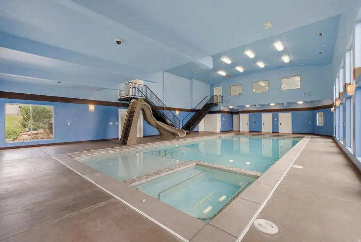 Indoor swimming pool featuring an integrated spa, concrete deck, and a waterslide with staircase access