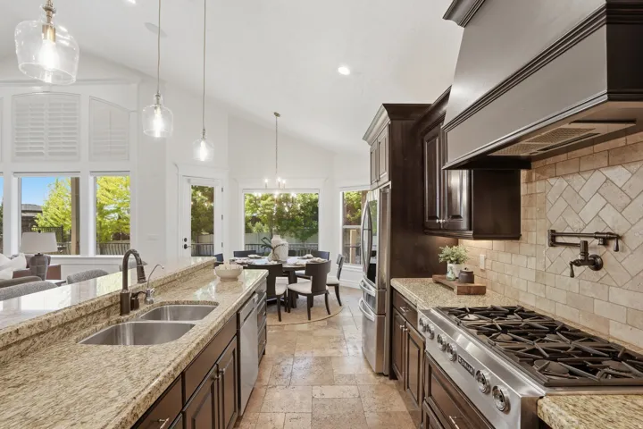 Gourmet kitchen featuring granite countertops, stainless steel appliances, a pot filler, and herringbone tile backsplash