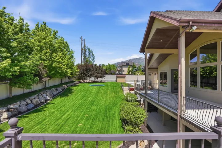 Expansive rear yard with manicured lawn, established perimeter trees, and a rock retaining wall