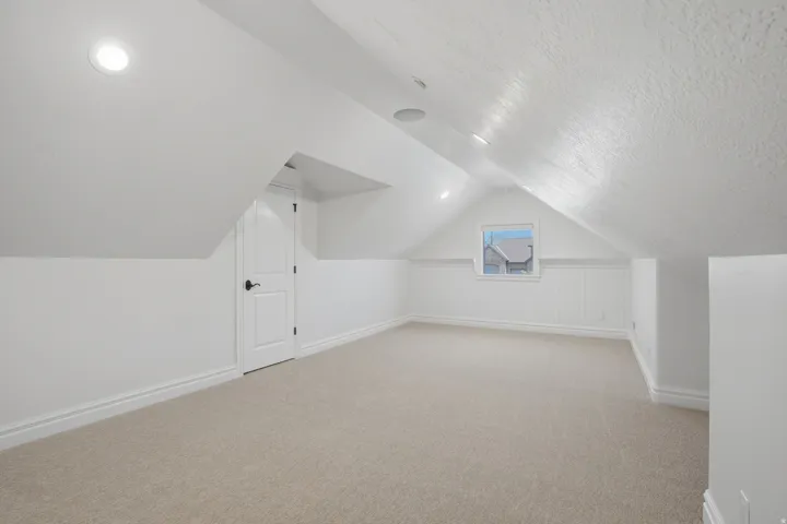 Carpeted attic space with sloped ceilings, recessed lighting, beadboard wall paneling, and a single window