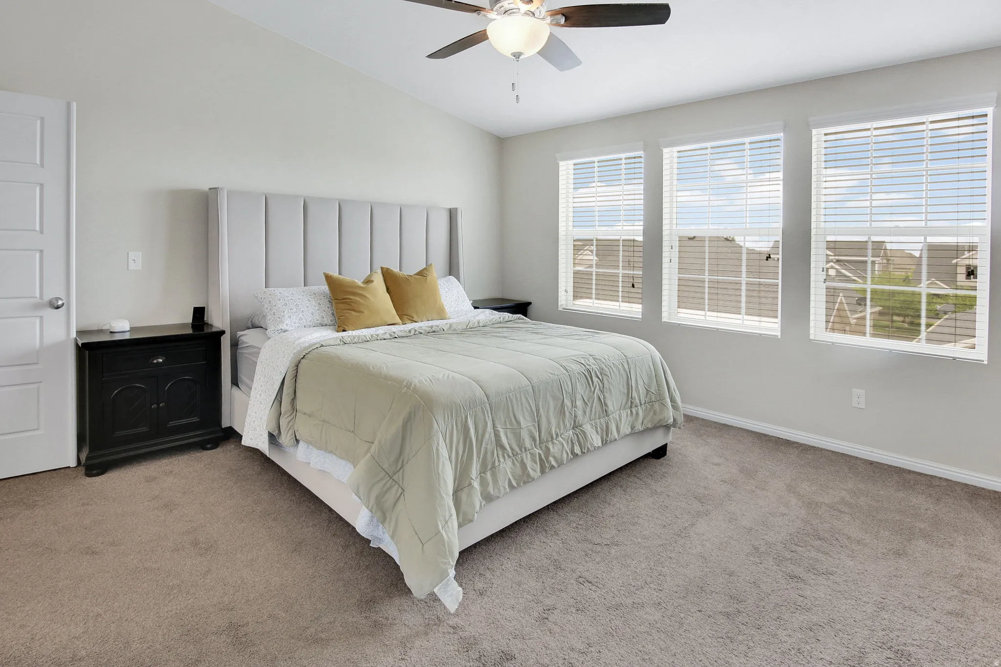 Carpeted room featuring a ceiling fan with integrated lighting, three windows with horizontal blinds, and an interior door with paneled design