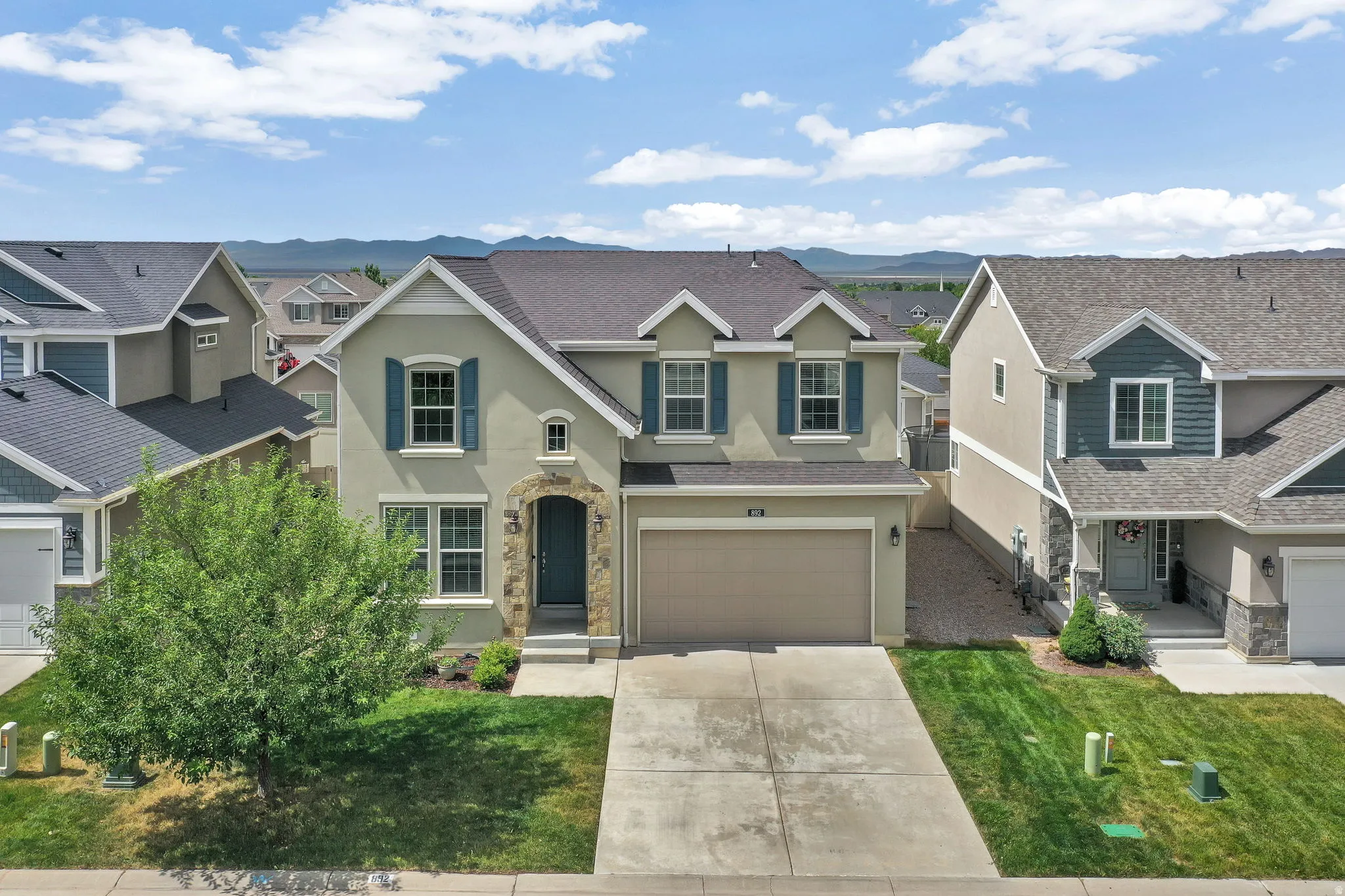 Two-story residence featuring a neutral stucco exterior with decorative blue shutters and stone accents around the entryway