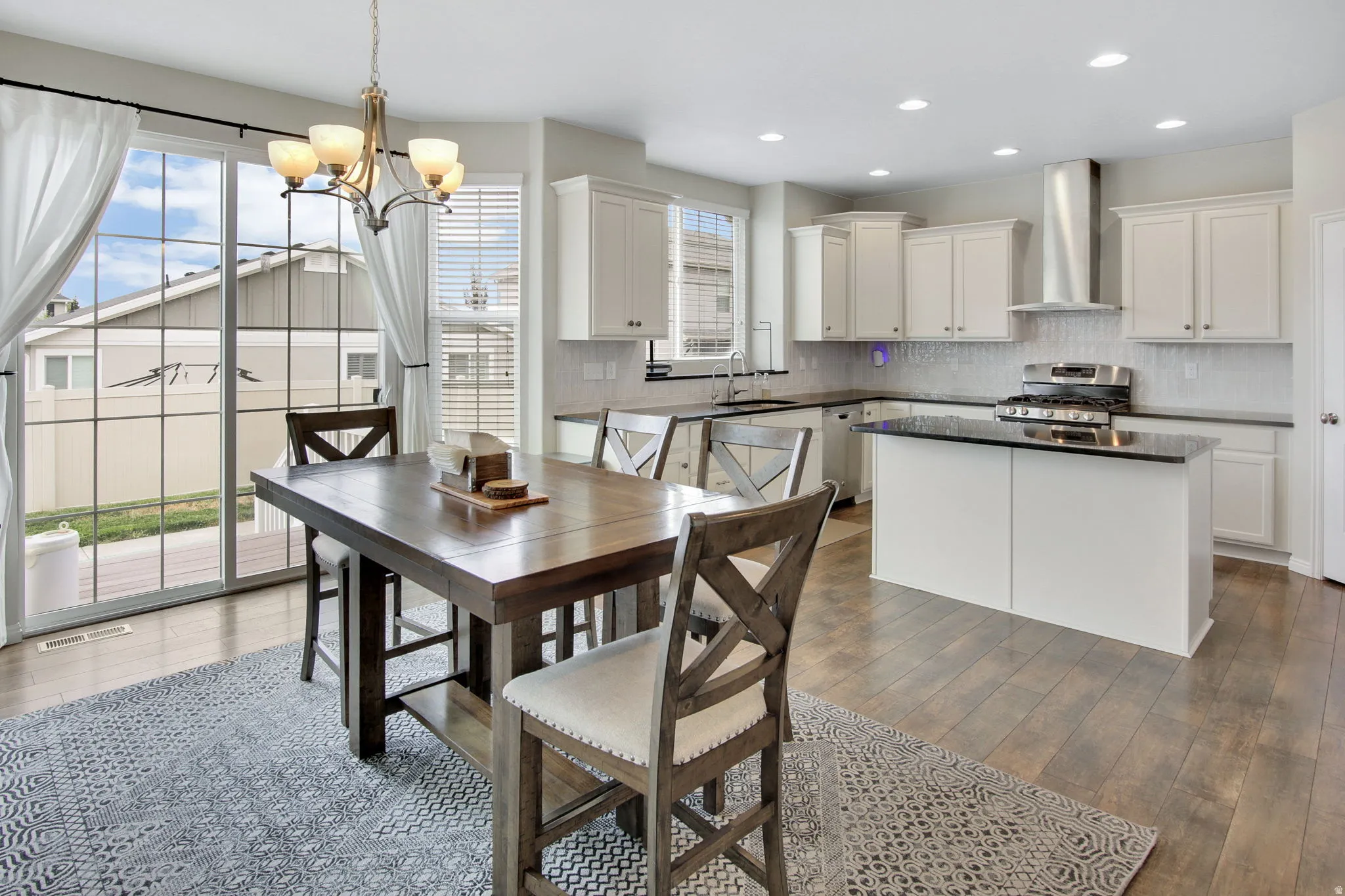Open-concept kitchen and dining area featuring wood-finish flooring, white cabinetry, a kitchen island with dark countertops, stainless steel appliances, and glass sliding doors