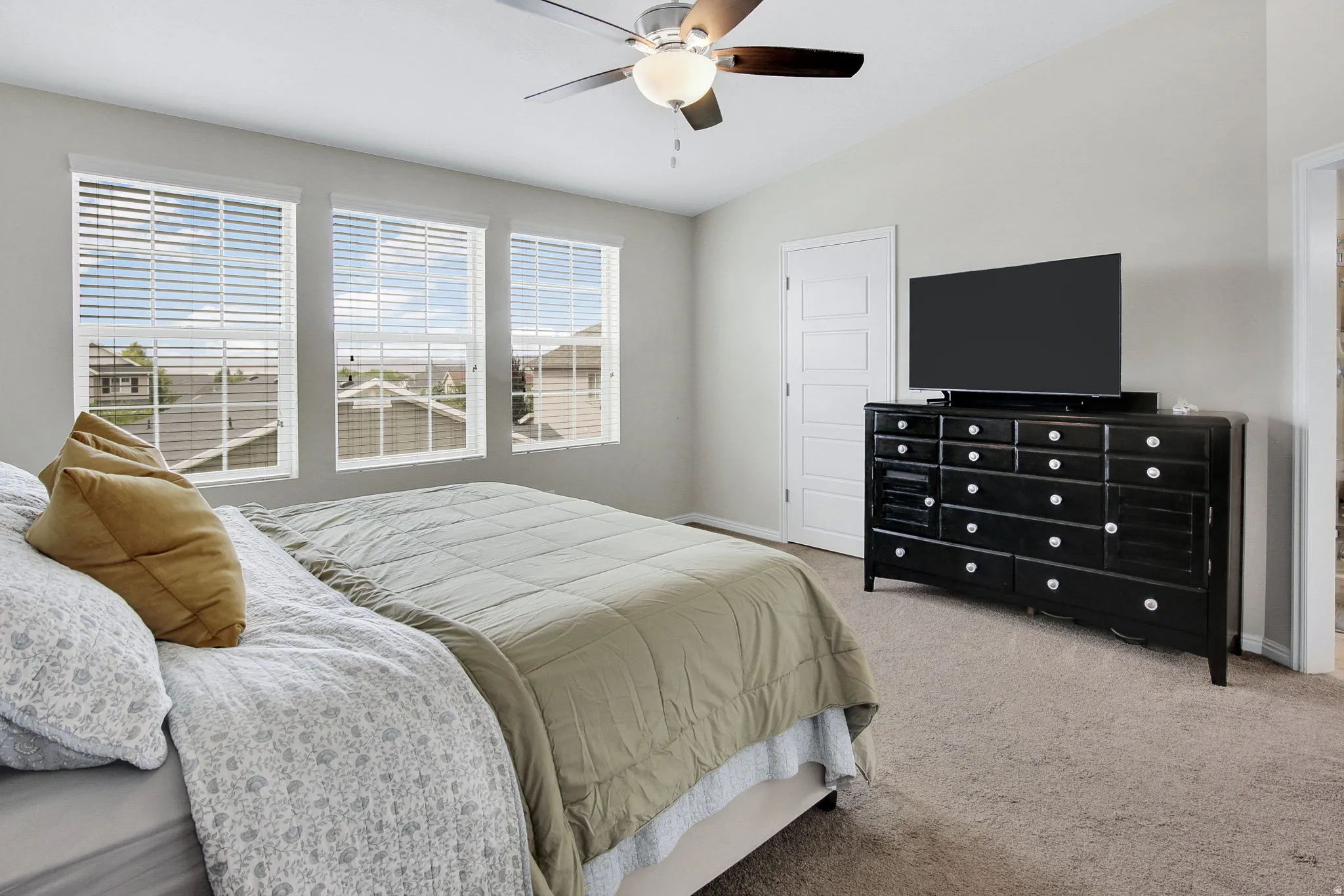 Spacious room featuring three windows with blinds, a vaulted ceiling, a ceiling fan with light fixture, and neutral carpet flooring