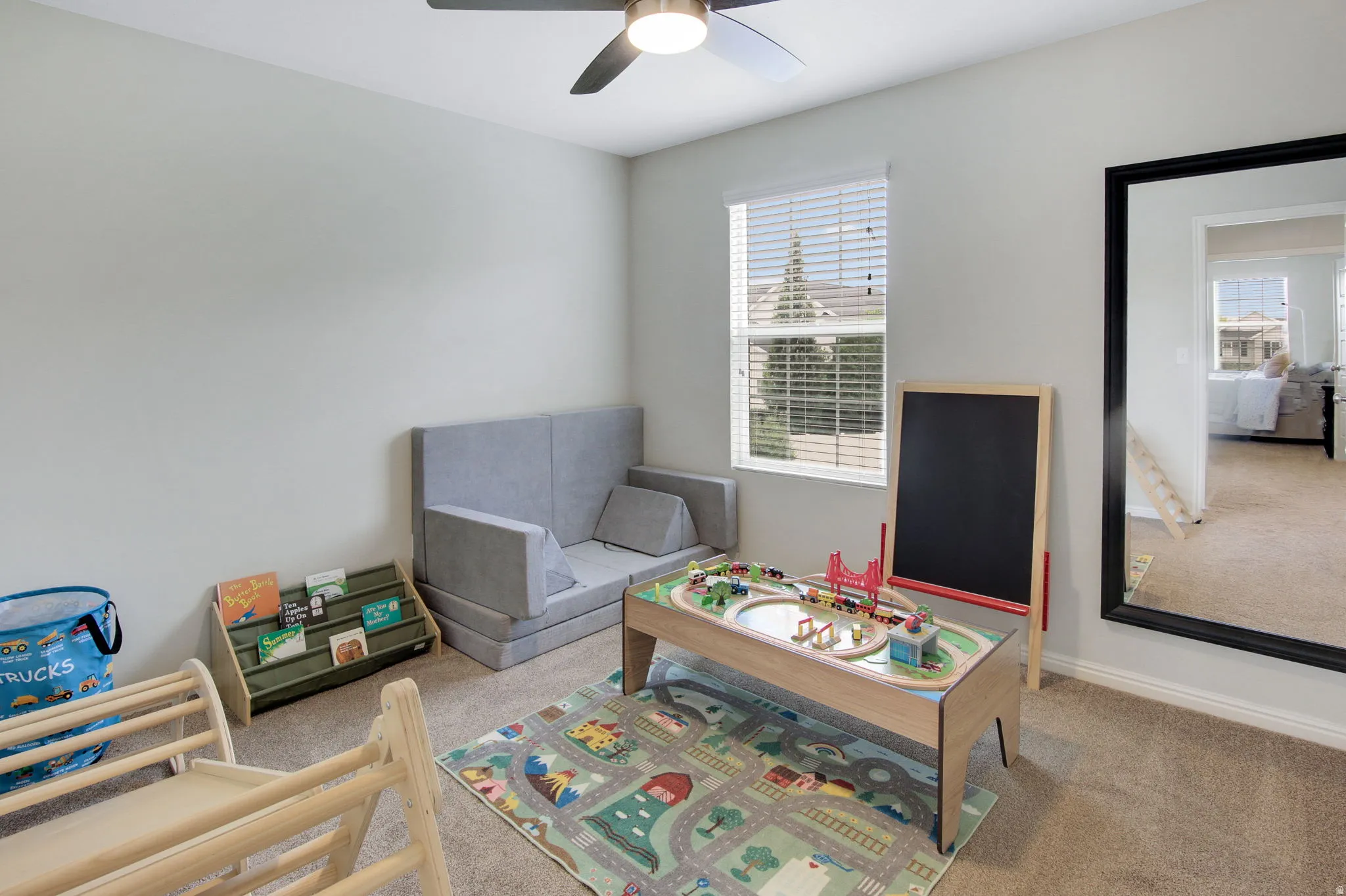 Carpeted room featuring a ceiling fan with integrated lighting, a window with horizontal blinds, and a large wall-mounted mirror