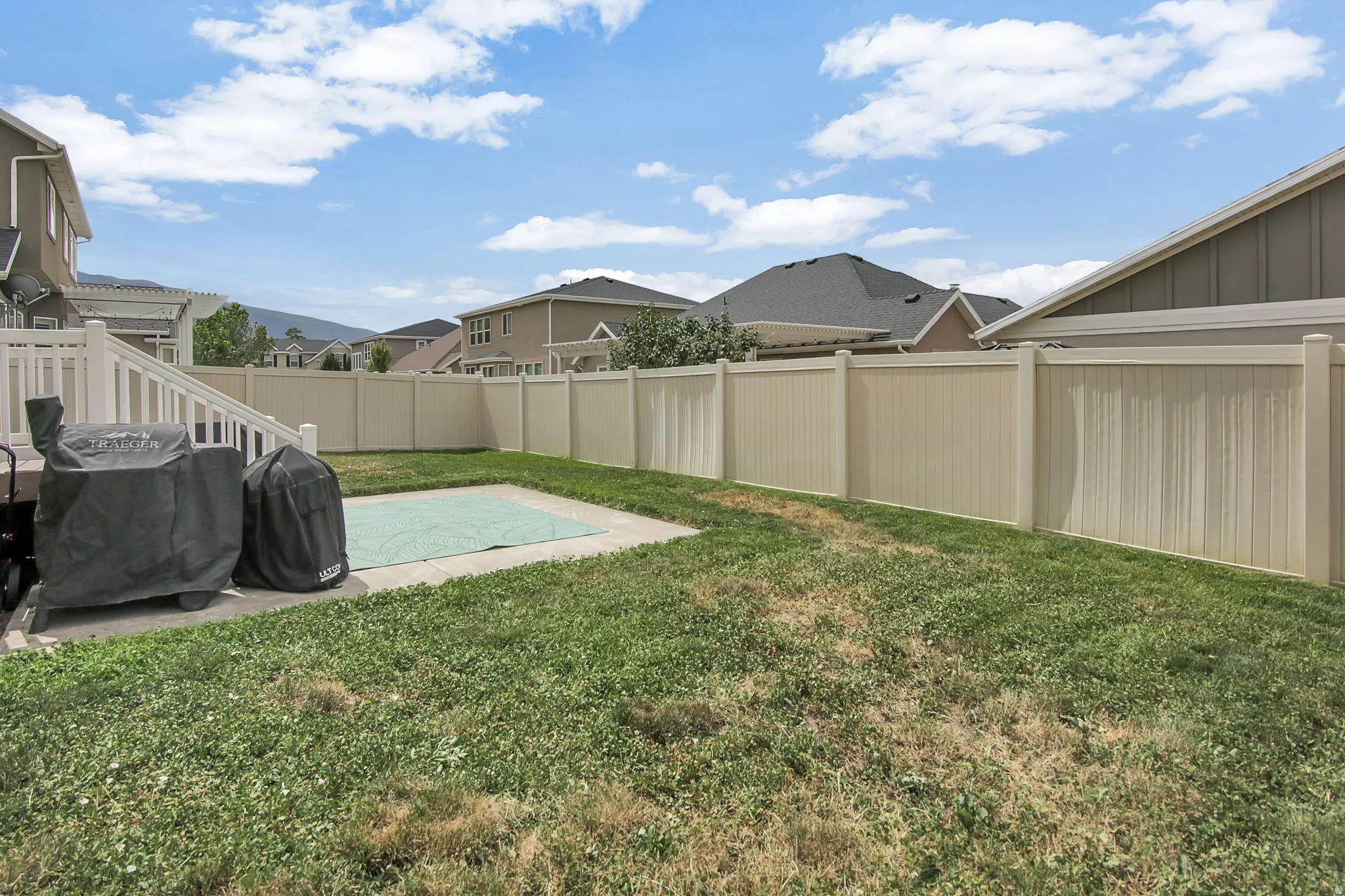 Spacious backyard featuring a concrete patio area, a grass lawn, and a light-colored privacy fence