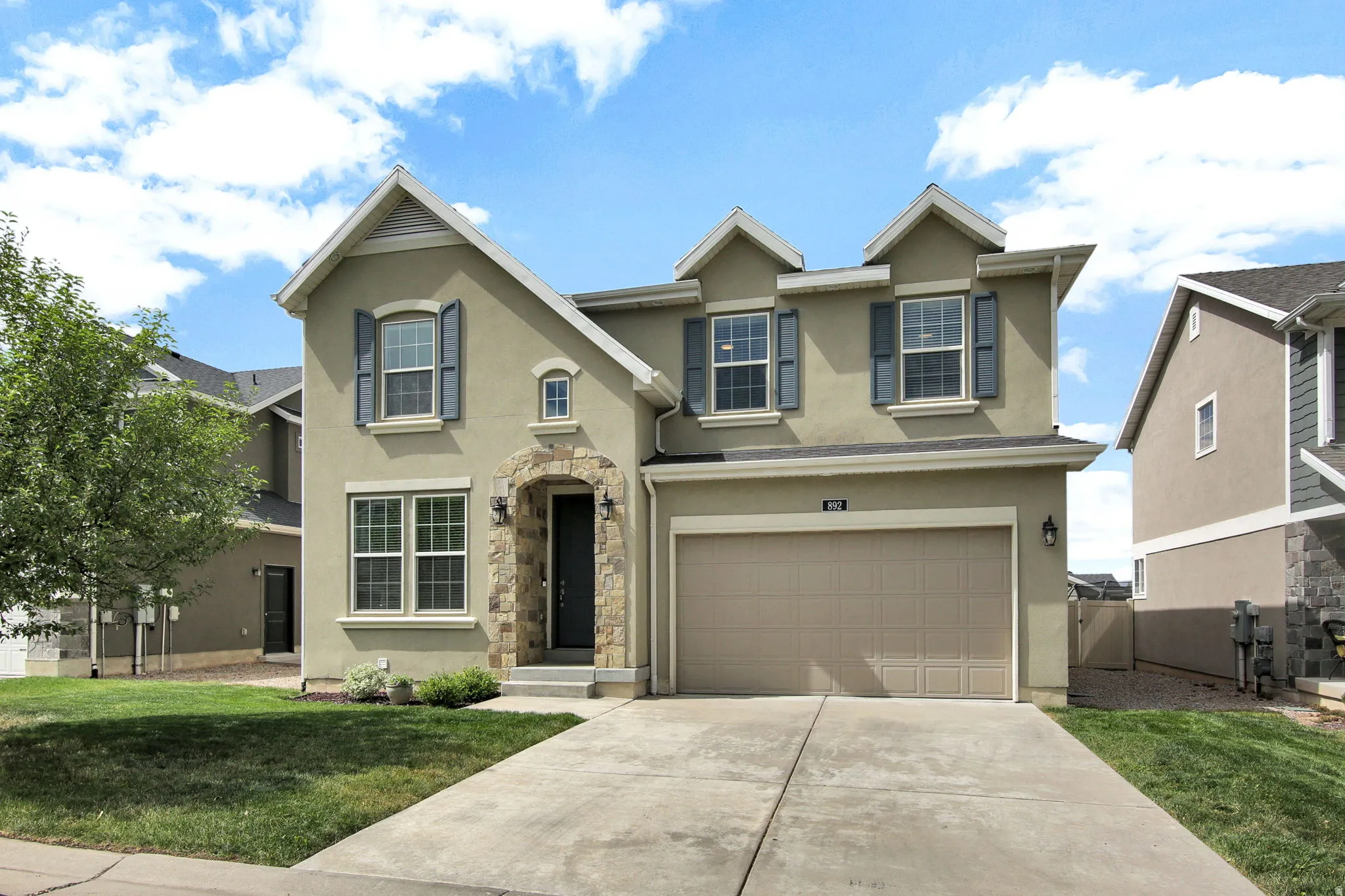 Two-story residence featuring a neutral stucco exterior, stone archway entry, and attached two-car garage