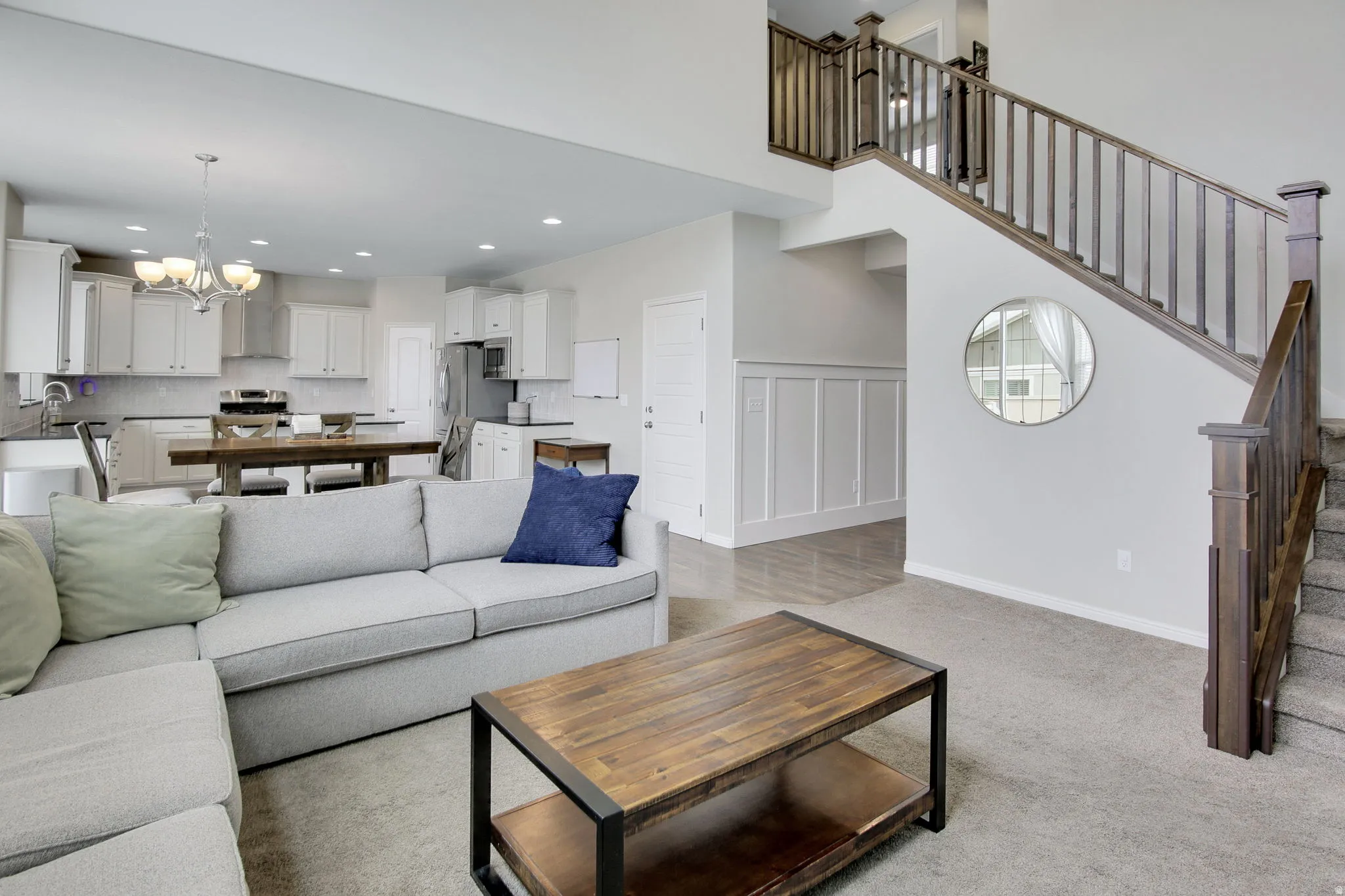 Open-concept living space featuring a two-story staircase with dark wood banisters, recessed lighting, and light gray wall paneling