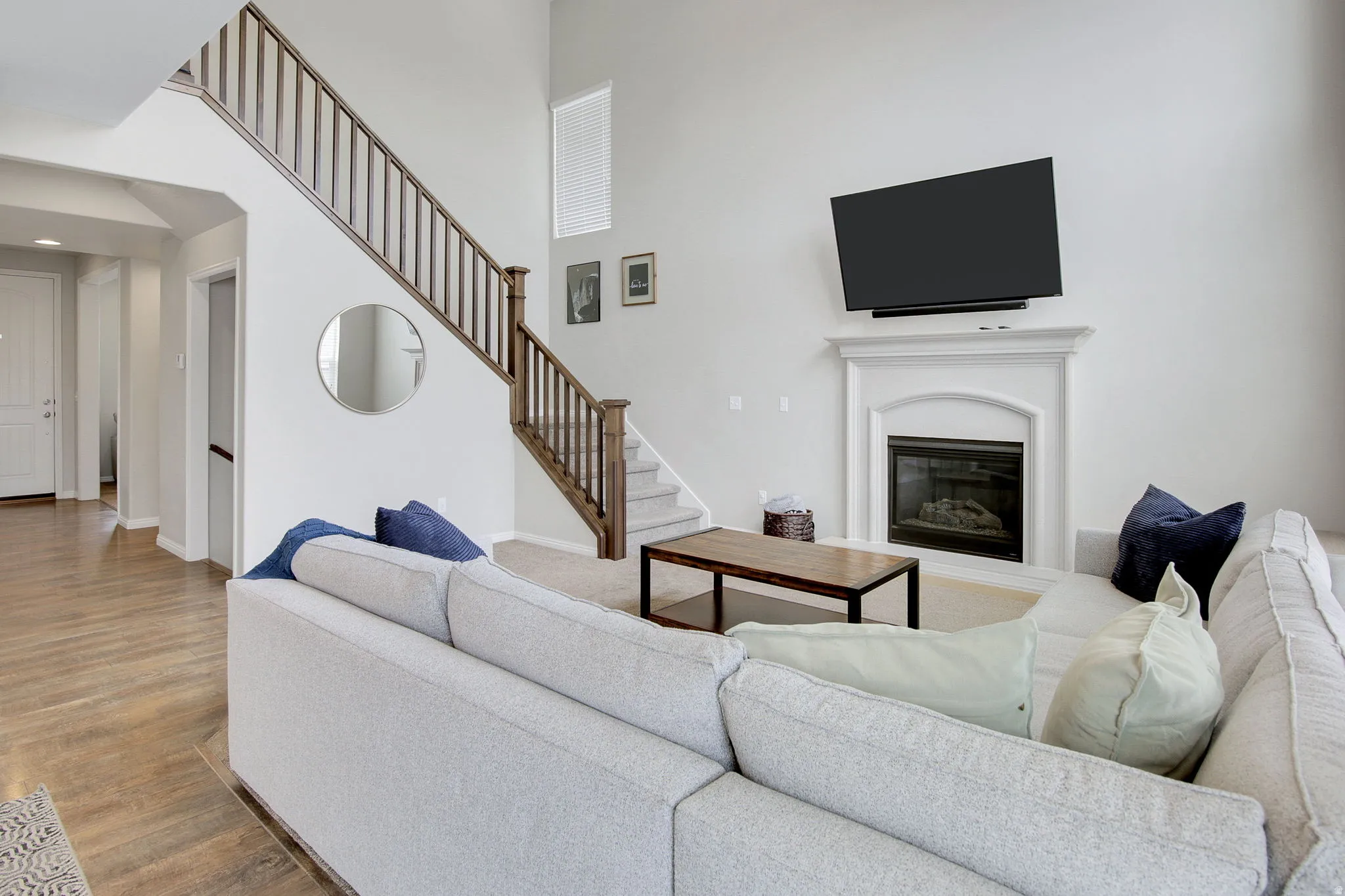Vaulted ceiling living space featuring a fireplace with a white mantel, an open staircase with wood banisters, and wood-finish flooring
