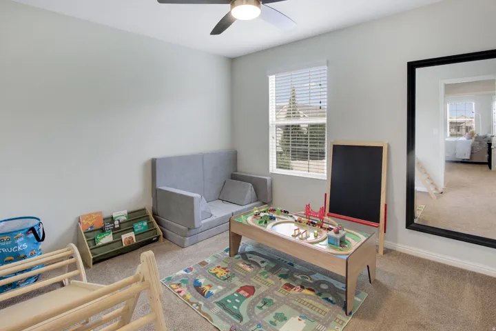 Carpeted room featuring a ceiling fan with integrated lighting, a window with horizontal blinds, and a large wall-mounted mirror