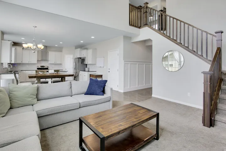 Open-concept living space featuring a two-story staircase with dark wood banisters, recessed lighting, and light gray wall paneling