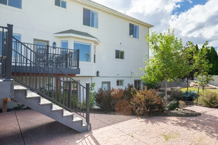 Rear exterior featuring a composite deck with metal railings and stairs, a bay window, and a stamped concrete patio