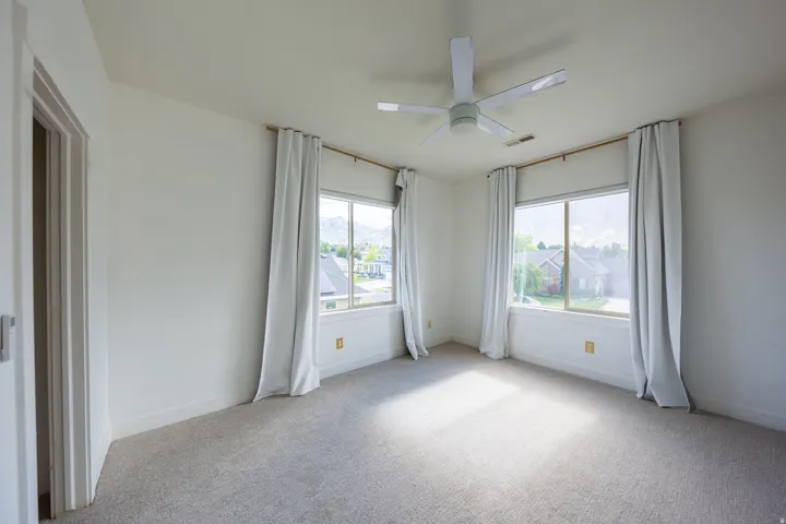 Bright room featuring two large windows, a ceiling fan, and light-toned carpeting