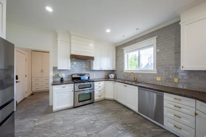 Kitchen featuring white cabinetry with gold-toned hardware, dark stone countertops, and a gray subway tile backsplash